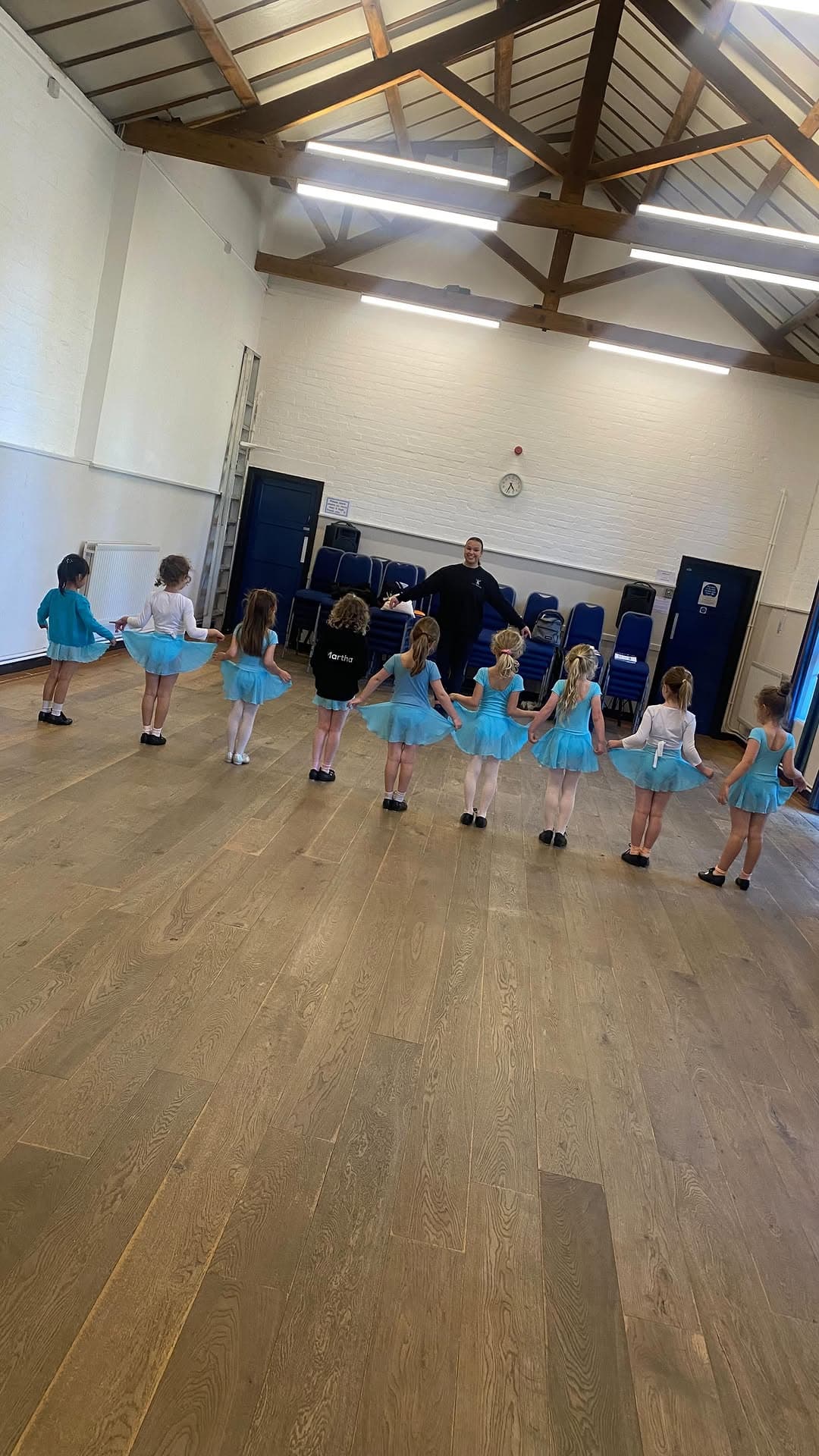 Young ballet students in blue skirts dancing in a line with their teacher